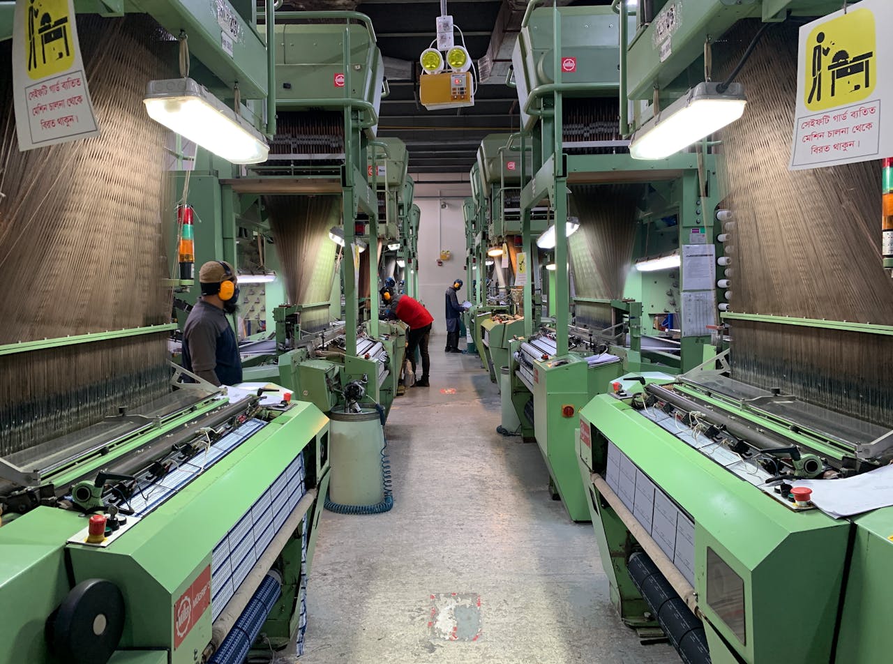 Industrial production line in Narayanganj, Bangladesh with workers at textile machines.