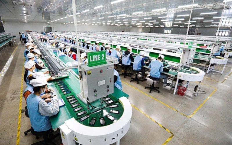 Factory workers seated at workstations on a production line in a Vietnamese manufacturing facility.